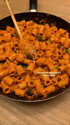 a skillet filled with pasta and vegetables on top of a wooden table next to a spoon