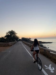 a woman is riding her bike down the road by the ocean at sunset or dawn