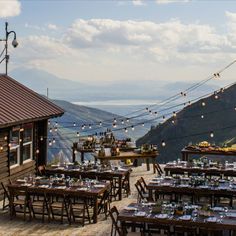 an outdoor dining area with tables and chairs overlooking the mountain range in the distance is lit by string lights