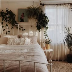 a white bed sitting in a bedroom next to a window with plants on the wall