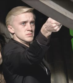 a man with blonde hair and blue eyes is holding something in his hand while another person looks on