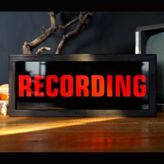 a black and red sign that reads recording sitting on a table next to a tv