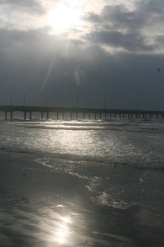 the sun shines brightly in front of an ocean beach with a long pier on it