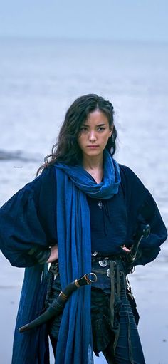 a woman dressed in pirate garb standing on the beach with her arms around her waist