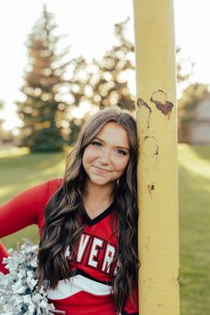 a cheerleader leaning against a pole with her pom poms