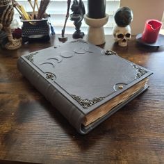 an open book sitting on top of a wooden table next to a vase and candles