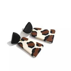 two pairs of black and white earrings with brown spots on the front, one is shaped like a cow's head