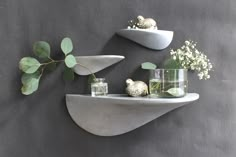 three white shelves with vases and plants on them against a gray wall behind it