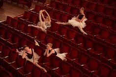 four ballerinas in black and white tutus are sitting on red velvet seats