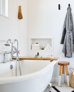 a white bath tub sitting in a bathroom next to a wooden stool and towel rack