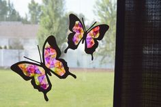 two stained glass butterflies sitting on top of a window sill in front of a grass field