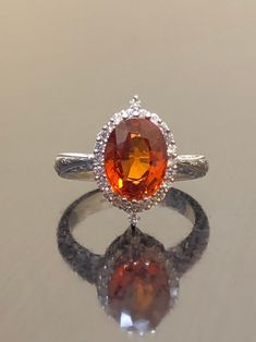 DeKara Designs Collection Our latest design! An elegant and lustrous Opal cabochon and diamond hand engraved platinum engagement ring. Metal- 90% Platinum, 10% Iridium. Stones- Genuine Oval Orange Sapphire 2.50 Carats. 24 Round Diamonds F-G Color VS1-VS2 Clarity 0.25 Carats. Latest of my creations! A Beautiful Handmade Hand Engraved Orange Sapphire Halo Diamond Engagement Ring Made in Platinum. The fiery Orange Sapphire is oval in shape and professionally prong set in between two unique triple p Luxury White Gold Topaz Ring With Halo Setting, Luxury 14k White Gold Topaz Wedding Ring, Elegant Orange Sapphire Round Ring, Luxury Wedding Topaz Ring With Halo Setting, Luxury Topaz Wedding Ring With Halo Setting, Luxury Topaz Ring With Halo Setting For Wedding, Orange Brilliant Cut Jewelry For Weddings, Formal Orange Diamond Ring, Wedding Orange Brilliant Cut Jewelry