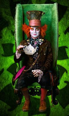 a creepy clown sitting in a green chair with a teapot on it's lap