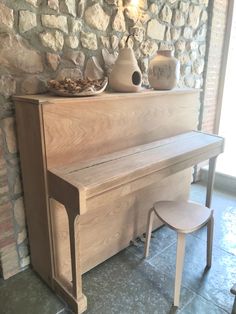 a wooden piano sitting in front of a stone wall with two stools next to it