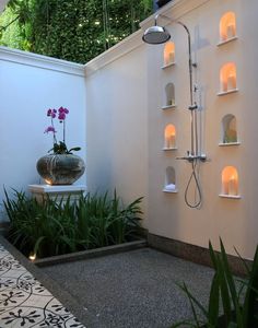 an outdoor shower with plants and candles on the wall next to it in a courtyard