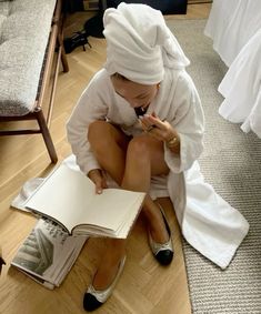 a woman sitting on the floor with a book in her hand and wearing a towel over her head