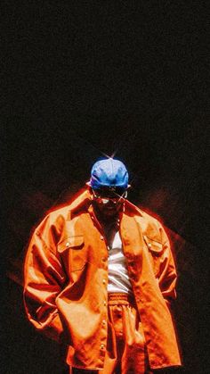 a man wearing an orange jacket and blue hat standing in front of a black background