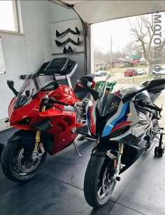 two motorcycles parked in a garage next to each other on the floor and one is red