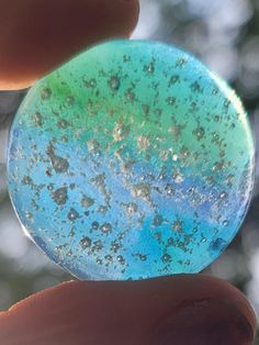 a hand holding a piece of glass with blue and green flecks on it