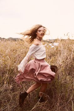 a woman in a dress is running through the grass with her hair blowing in the wind