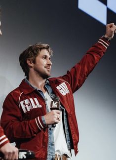 a man standing in front of a screen holding a microphone and wearing a red jacket