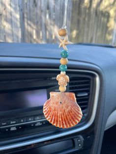 an orange shell hanging from the dashboard of a car with beads and seashells on it