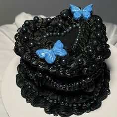 a black and blue cake with butterflies on it's top is sitting on a white plate