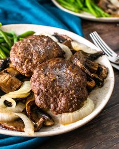 two hamburger patties with onions and mushrooms on a white plate next to green beans