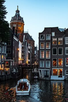 a boat traveling down a river next to tall buildings with lights on it's windows