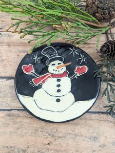 a black and white plate with a snowman painted on it next to pine cones