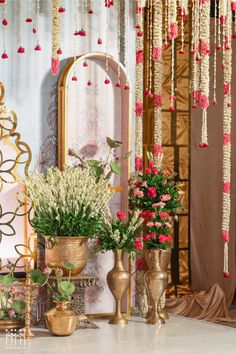 a table topped with vases filled with flowers next to a wall covered in hanging decorations