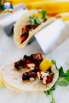 two tacos with meat, pineapple and cilantro on them sitting on a table