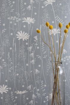 some yellow flowers in a clear vase on a table next to a wallpapered wall