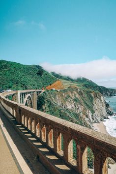 a long bridge over the ocean next to a cliff with waves crashing on it's sides