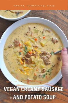 a person holding a spoon over a bowl of soup with sausage and potato soup in it