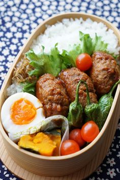 a wooden bowl filled with meatballs, rice and veggies on top of a blue table cloth