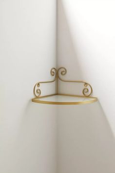 the corner of a white room with a gold shelf