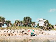 an umbrella is sitting on the beach next to some palm trees and a lifeguard tower