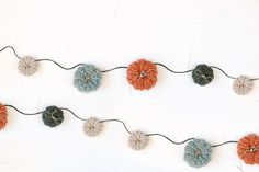 crocheted pumpkins are hanging from a string on a white wall with black cord