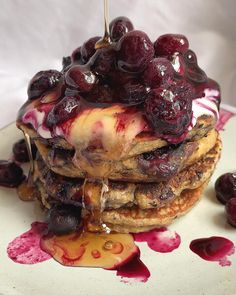 a stack of pancakes topped with fruit and syrup on top of a white plate next to cherries