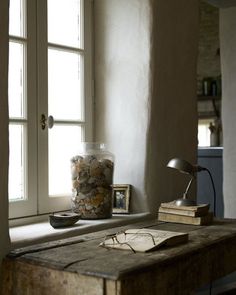 an old desk with a lamp, books and other items on it in front of two windows