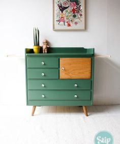 a green dresser sitting in front of a painting on the wall next to a potted plant