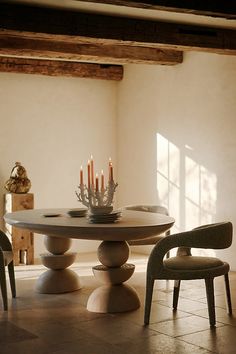 a dining room table with candles on top and chairs around it in front of a window