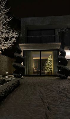 a house is lit up at night with snow on the ground and trees in front