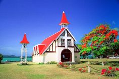 a small church with red roof and steeple next to the ocean on a sunny day