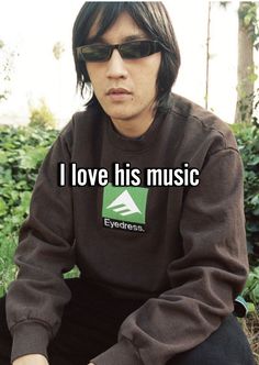 a man sitting on the ground in front of some bushes wearing sunglasses and a sweatshirt that says i love his music