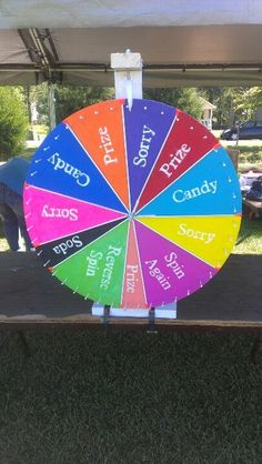 a colorful wheel of fortune sitting on top of a wooden table under a white tent