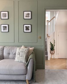 a grey couch sitting in front of a green wall with pictures hanging on the walls