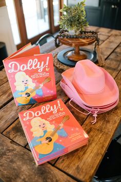 two children's books sitting on top of a wooden table next to a pink hat