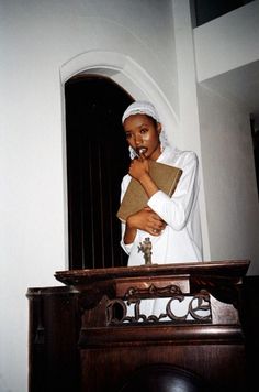 a woman dressed in white standing at a pulpit with her hands clasped to her chest